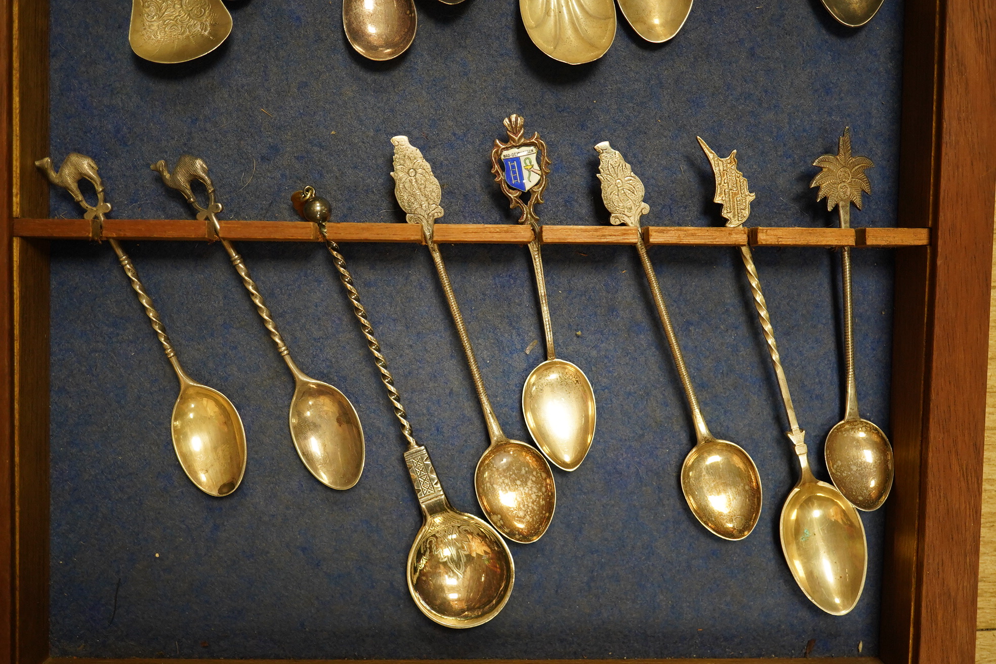 A quantity of collectors spoons from various countries, some silver with enamel, housed in a cabinet. Condition - fair